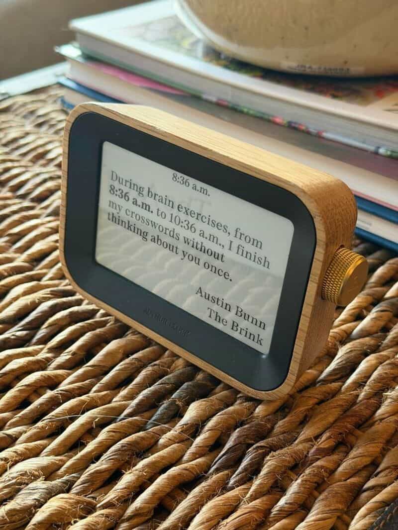 E-ink device on woven surface with books in background.