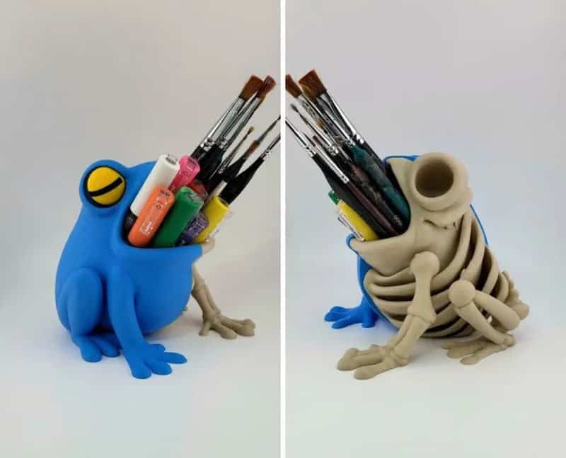Creative frog-shaped pen holder with art supplies, one in blue and one in beige.