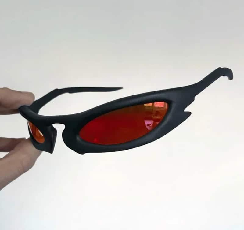 3D-printed black sunglasses with red lenses, held by a hand.