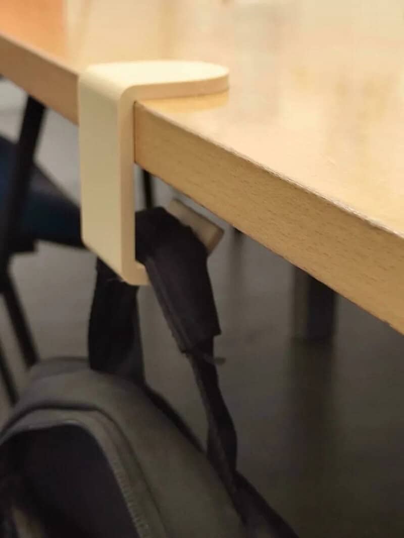 3D-printed hook holding a bag on a wooden table edge.