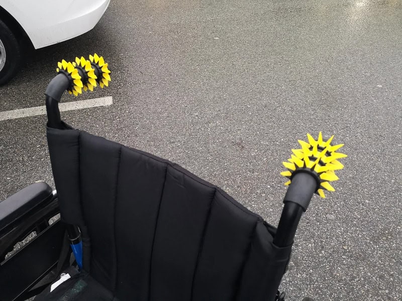 Black stroller with yellow spiked wheel protectors on parking lot surface.