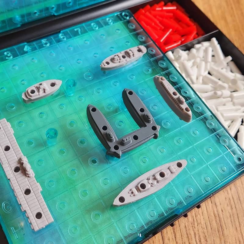 Board game with ships and red and white game pieces on a blue grid.