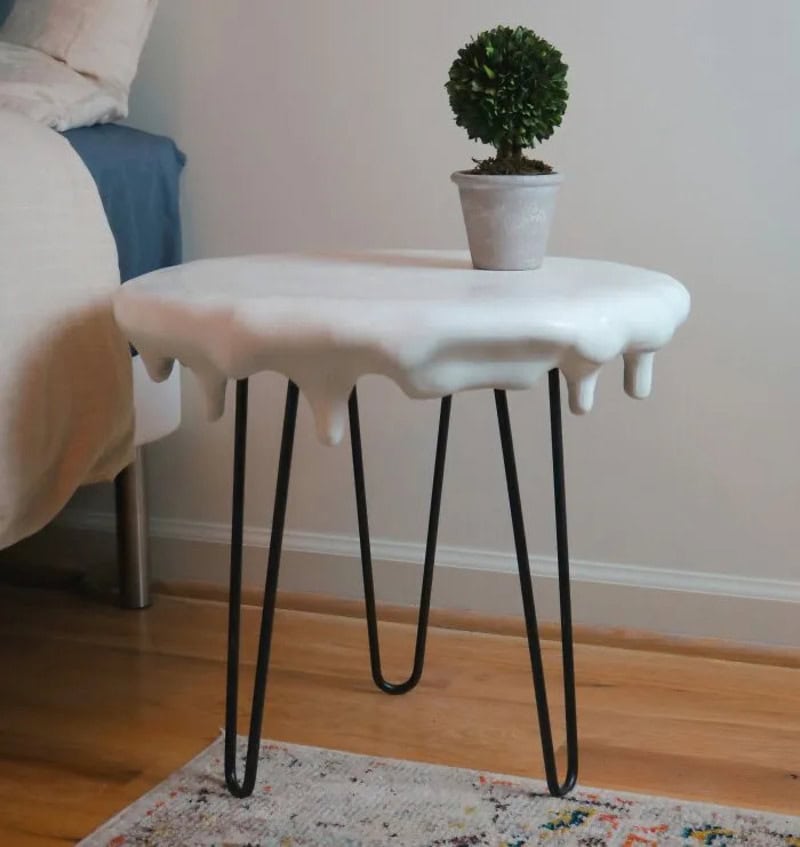 Side view of a small table with a melting ice cream cone shape and a potted plant on top.