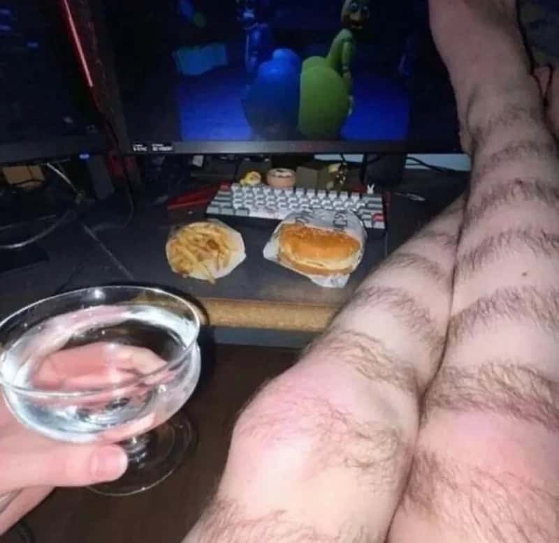 Person with hairy legs holding a glass of water in front of a computer with snacks and a cartoon on.