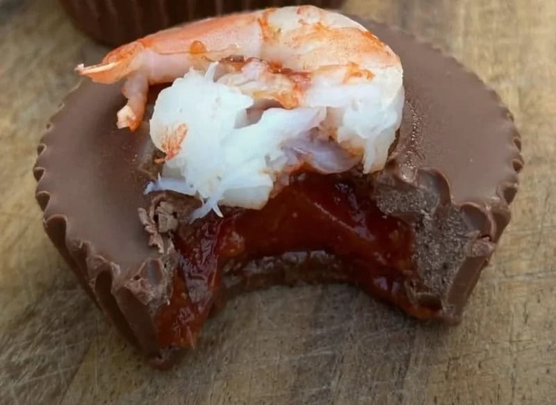 Chocolate dessert with shrimp, white cream, and red jam on top.