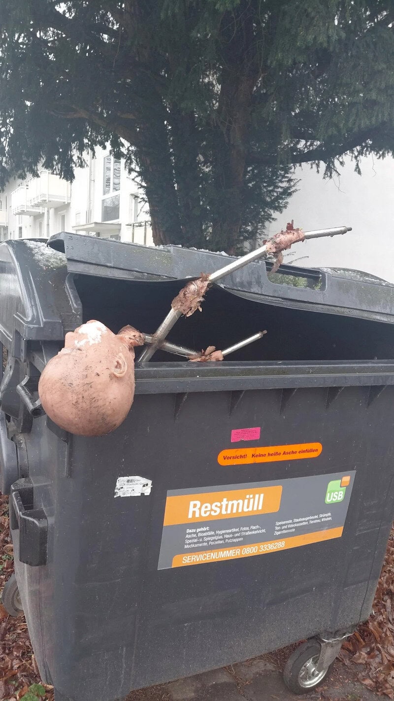 A trash bin with a strange object resembling a head and a stick protruding from it.
