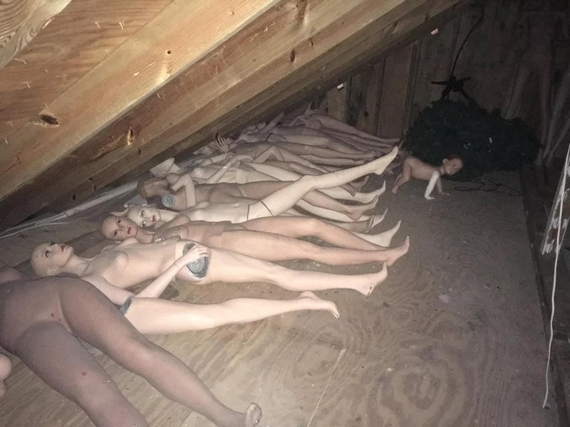 Multiple nude dolls lying on the attic floor with a small doll nearby.