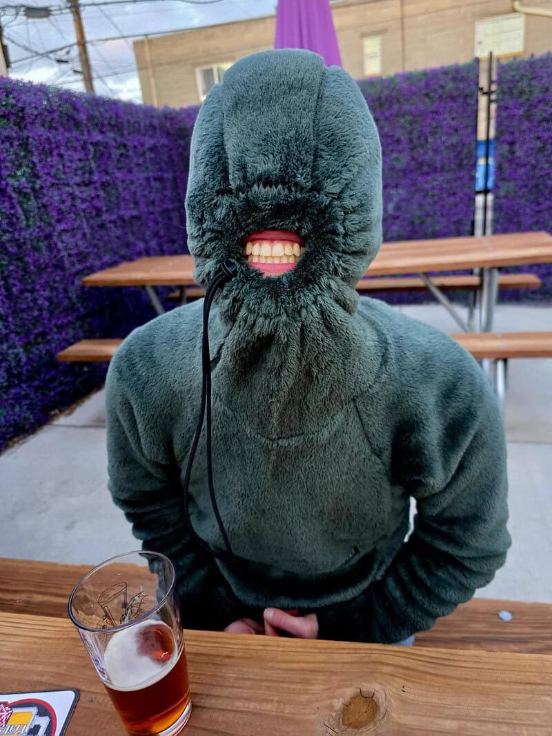 Person in a fuzzy hooded jacket with face covered, showing only teeth.