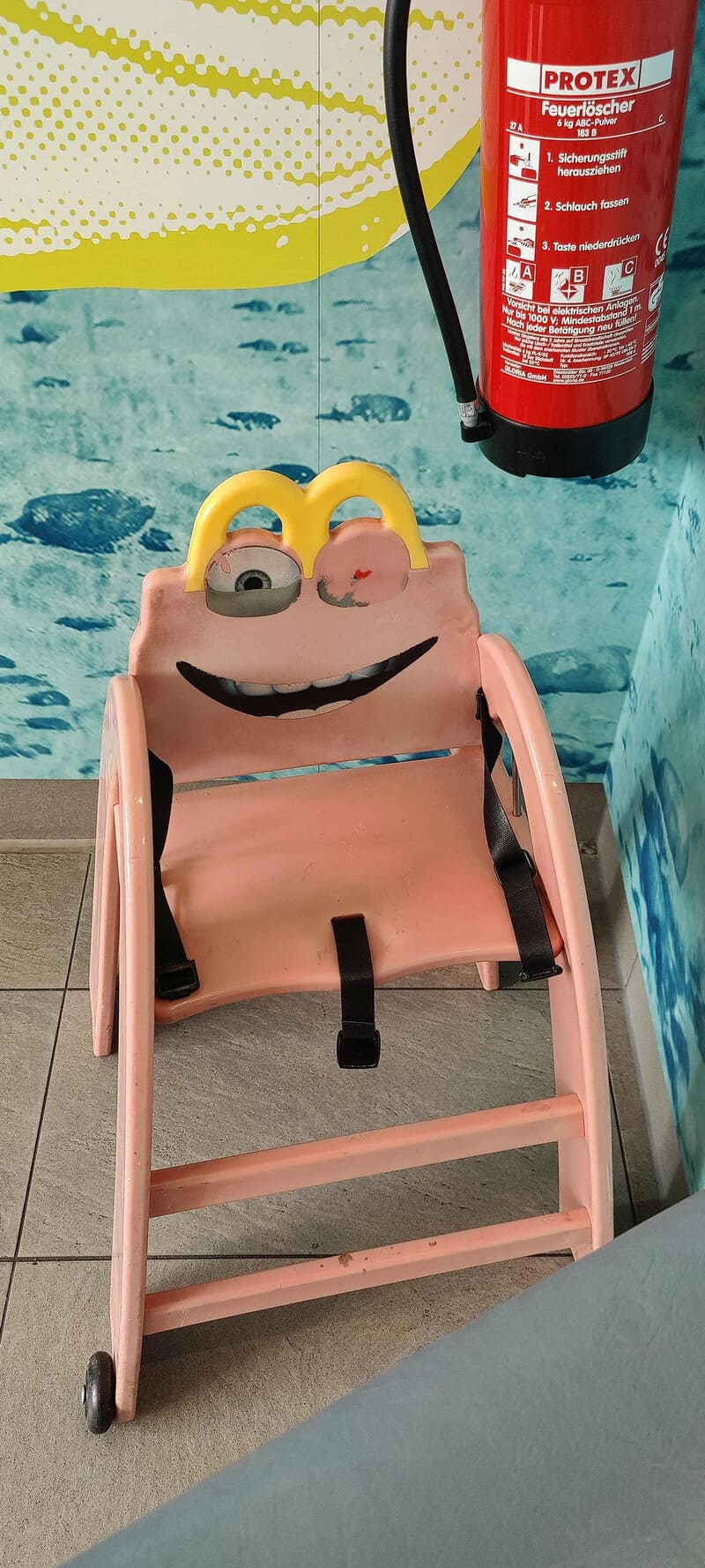 Pink children's chair with a SpongeBob SquarePants face and yellow eyes, near a pool and fire exting.