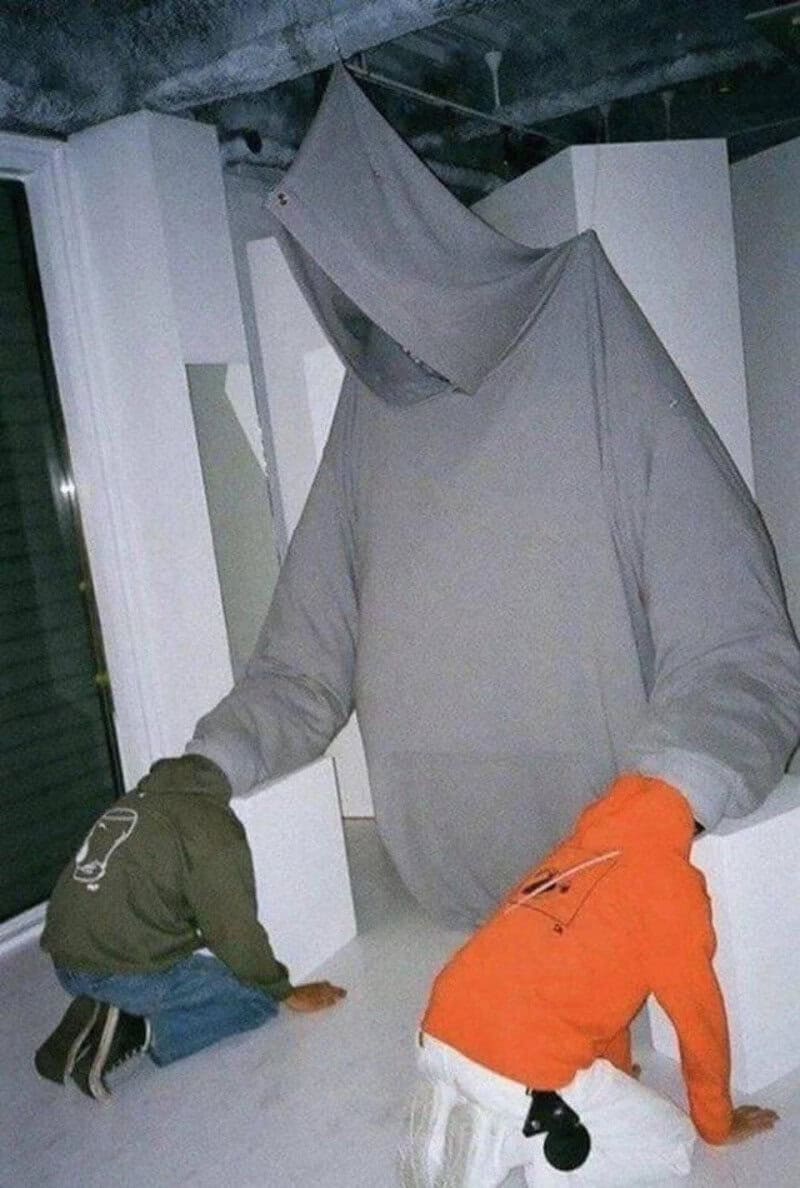 Figure with a hoodie and a cloth over the head, with two children crawling on the floor.