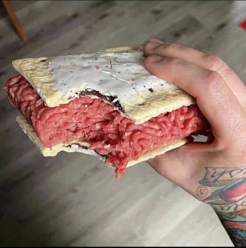 A hand holding a partially eaten dessert with pink filling and white icing.