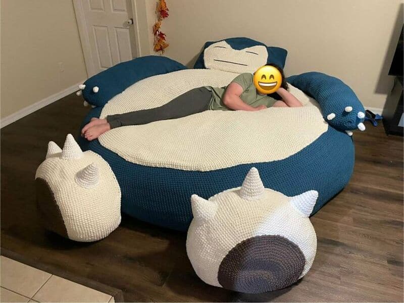 Child lying on a large, round, blue and white crochet unicorn bed with unicorn pillows.