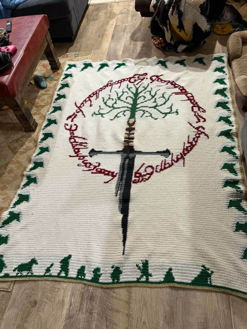 Crochet rug with a tree, sword, and circular text, on a wooden floor.