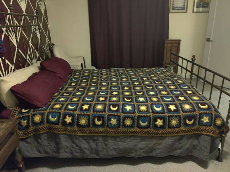 Crochet blanket with stars, moons, and hearts on a bed in a bedroom.