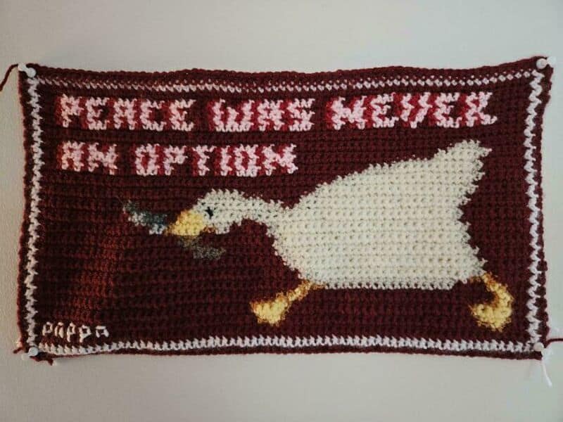Crochet rug with a white dog pulling a toy and text in red and white.