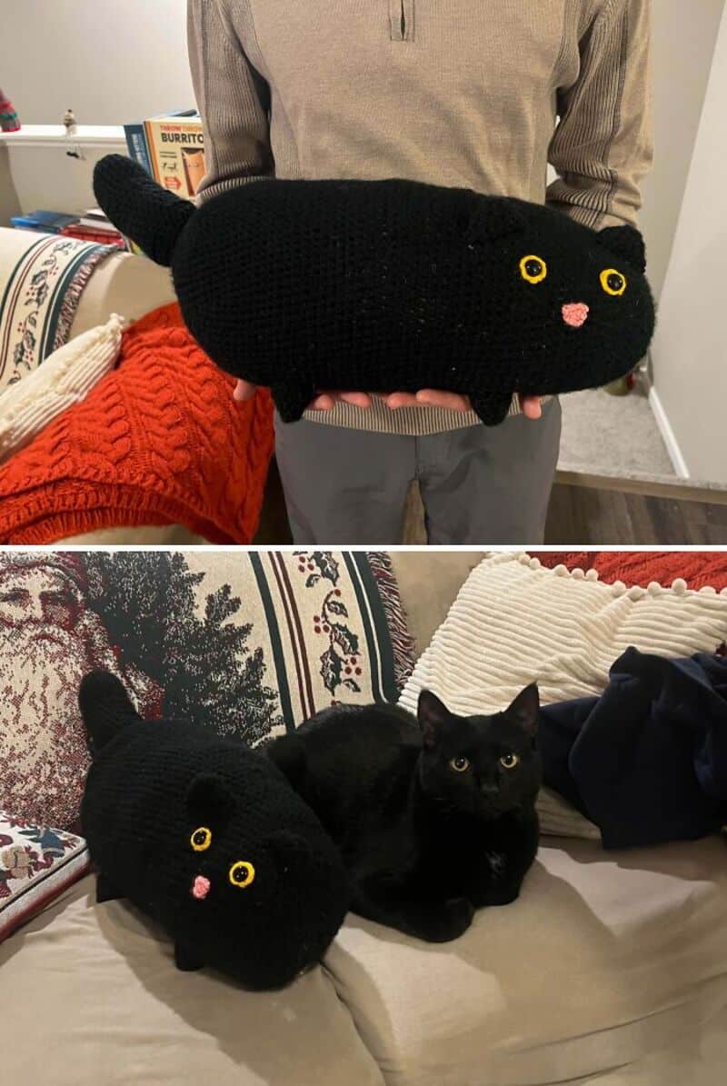 Black knitted cat-shaped pillow with yellow eyes and pink nose, held by a person.