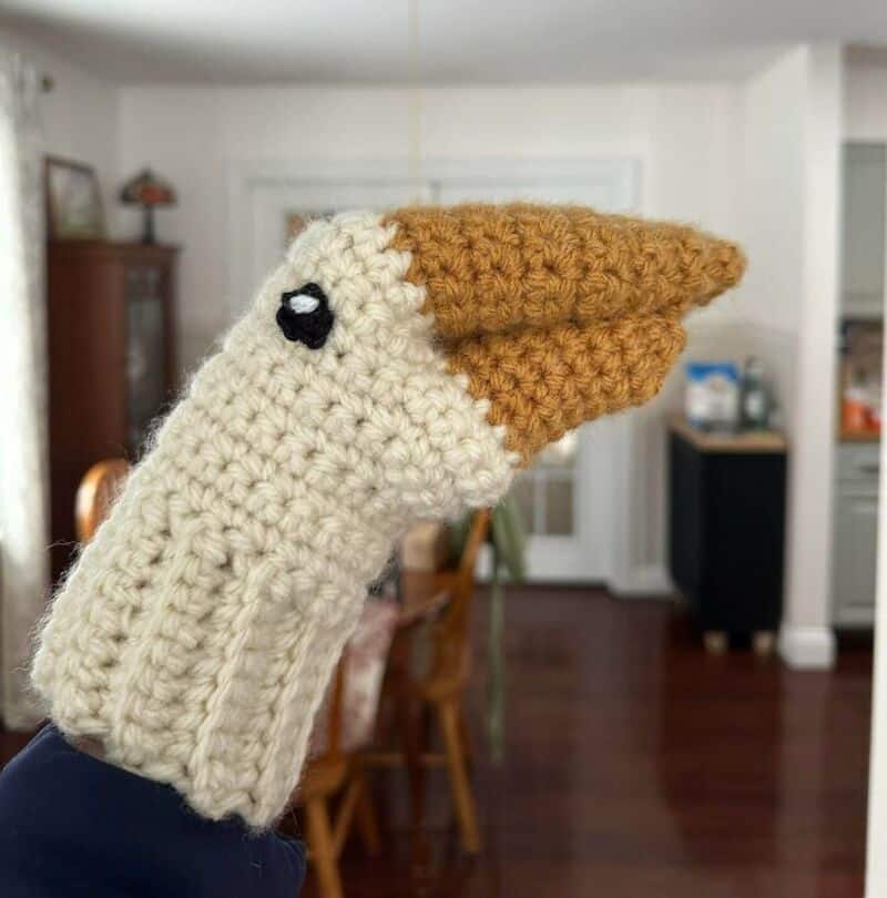 Crochet chicken puppet with beige body, brown beak, and black eye.