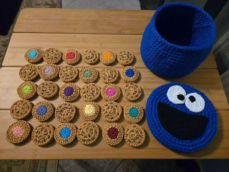 Crochet cookies and a Cookie Monster hat and face on a wooden table.