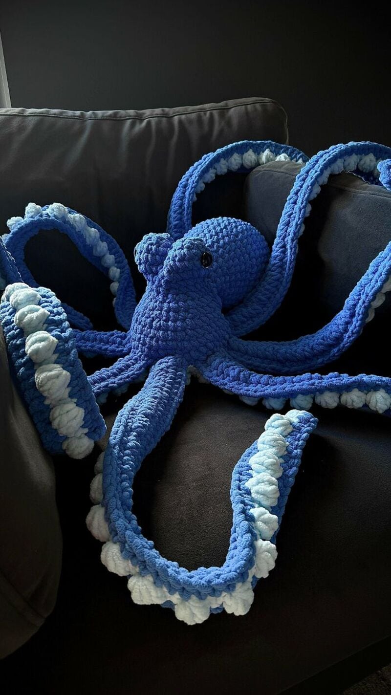 Blue crocheted octopus with white accents on a dark sofa.