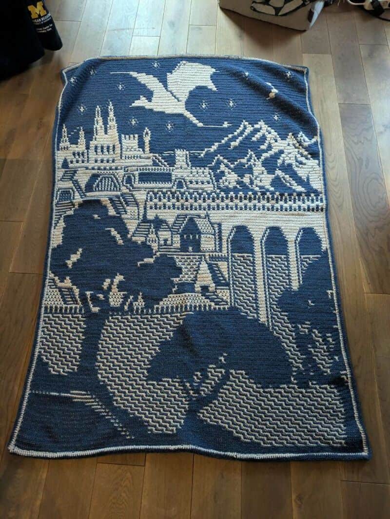 Crochet rug with a castle, mountain, bird, and landscape scene in blue and white.