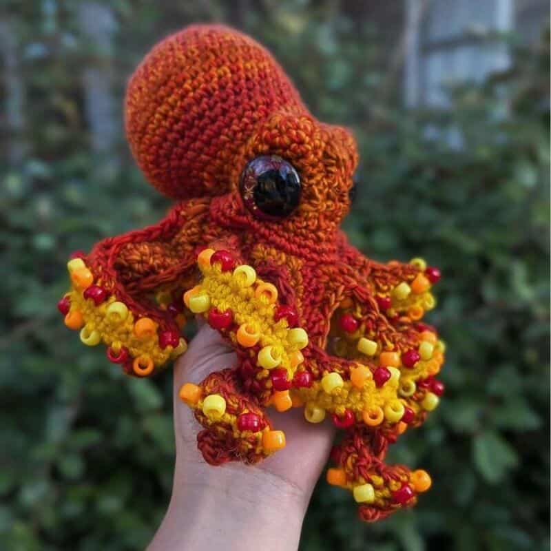 Colorful crocheted octopus with large black eyes, held outdoors.