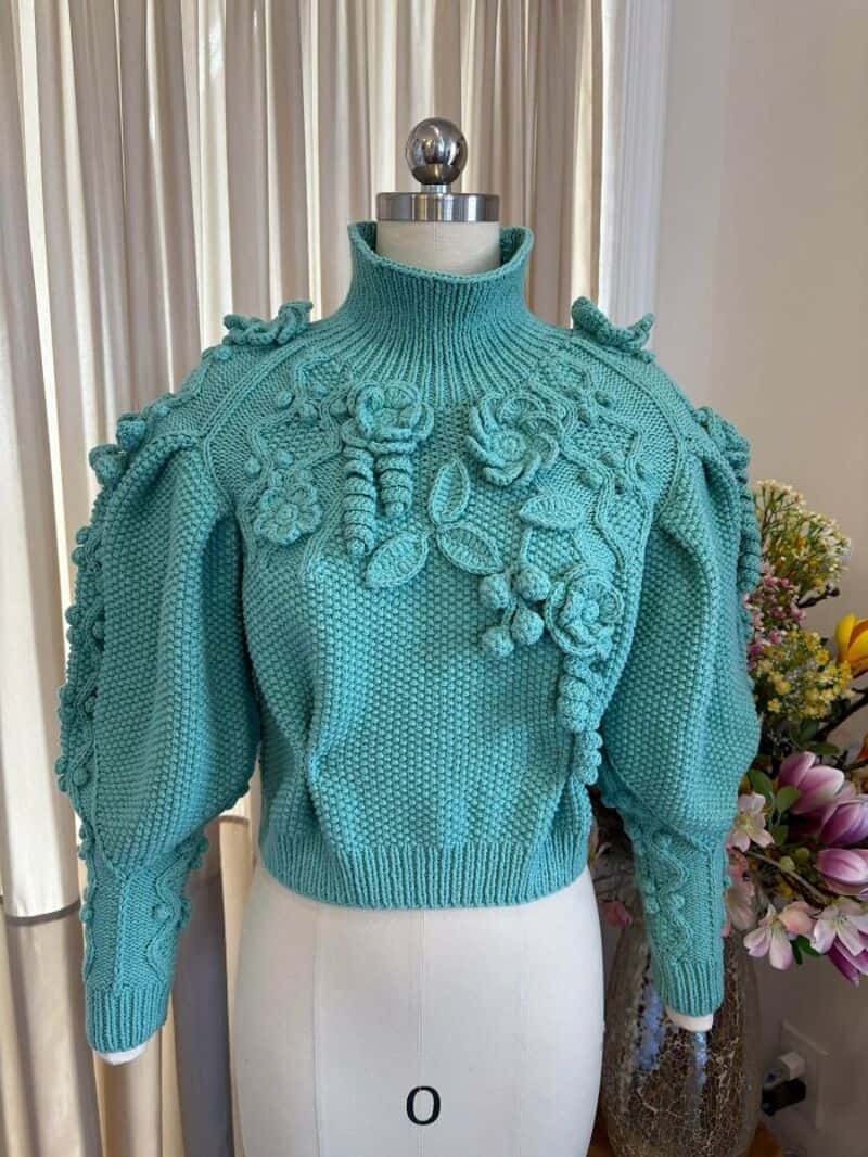 Turquoise crochet sweater with 3D floral details and puffed sleeves.