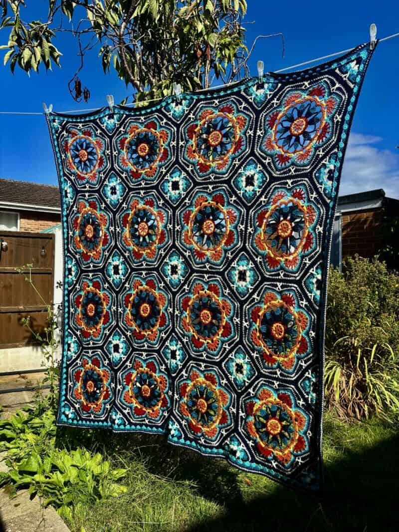 Colorful crochet blanket with floral patterns hanging outdoors on a sunny day.