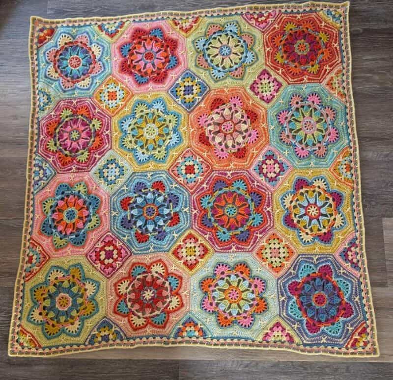 Colorful crochet blanket with hexagon and flower patterns on a wooden floor.