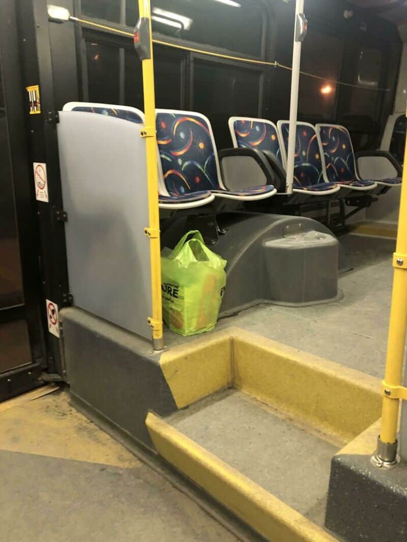 Empty bus seat area with a green bag and a gray container on the floor.