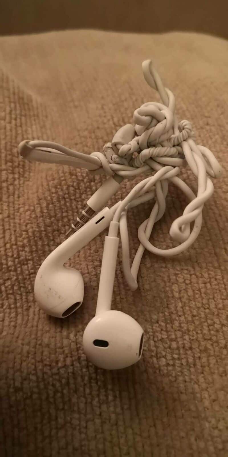 Tangled white earphones on a beige fabric surface.