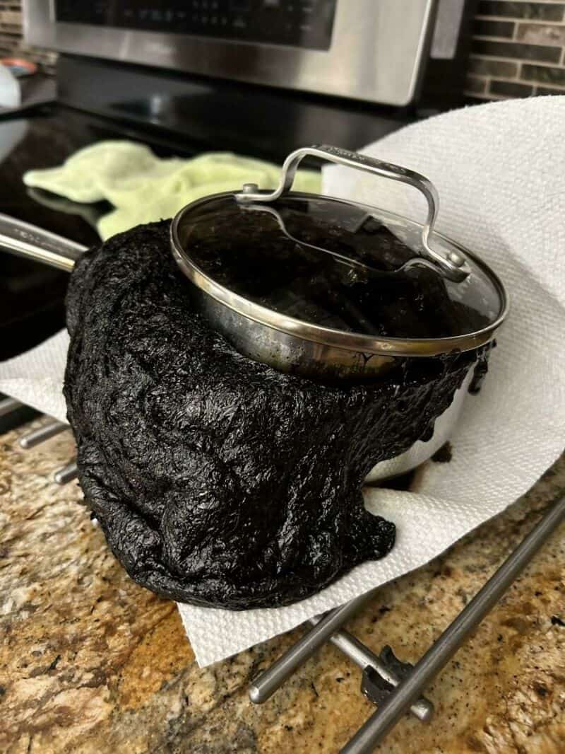 Burnt pot on a kitchen counter with a glass lid and a towel nearby.
