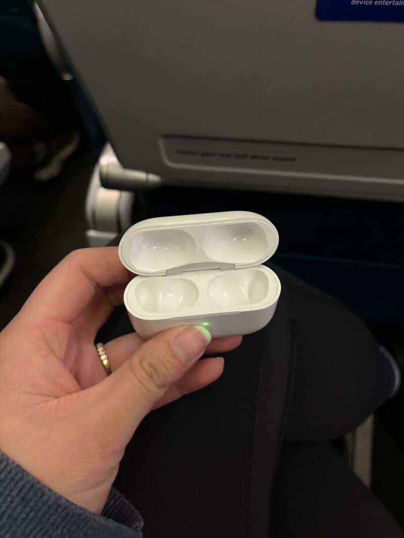 Empty wireless earbuds case held in hand on airplane seat.