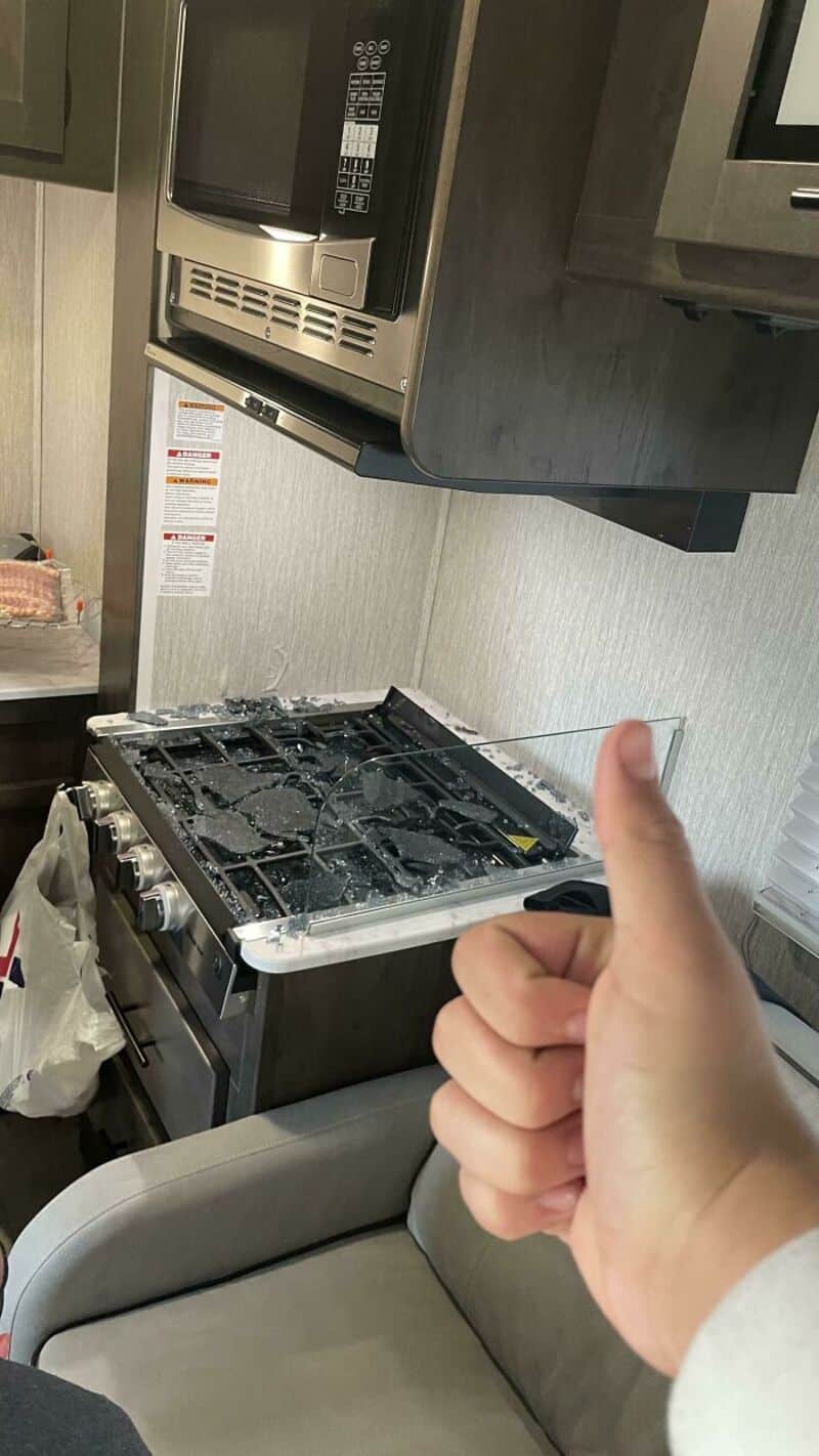 Thumbs up in front of a stove with no burners, in a kitchen.