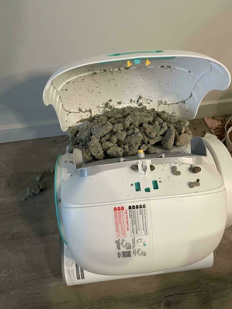 A broken rice cooker with spilled gray rice on the floor.