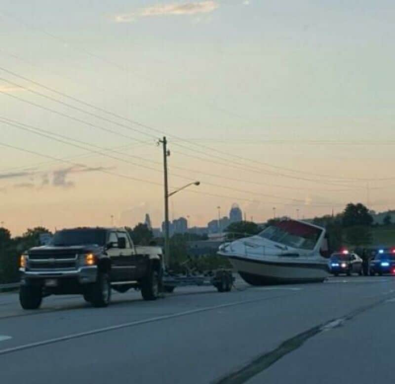 Boat on a trailer hitched to a pickup truck on the side of the road.