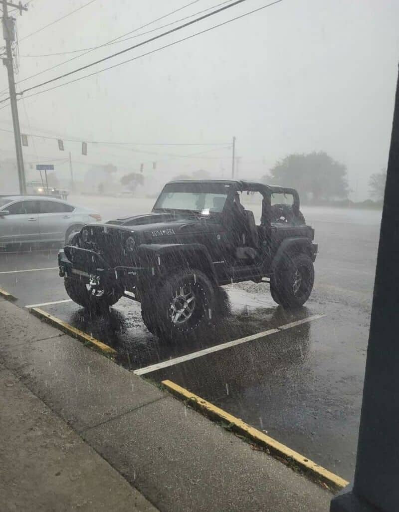 Jeep in a parking lot during a heavy rainstorm, with fog and water splashing.