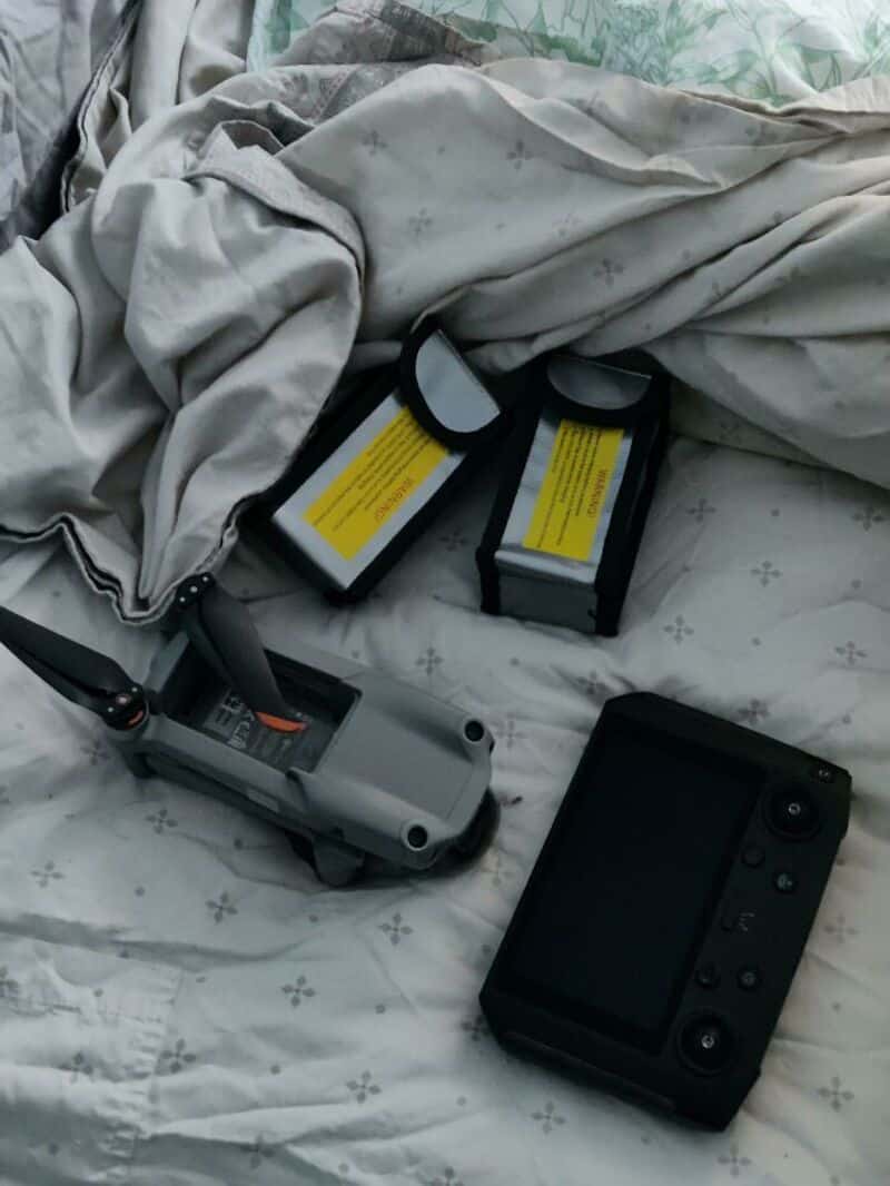 Drone, batteries, and camera on bed with sheets and blanket.