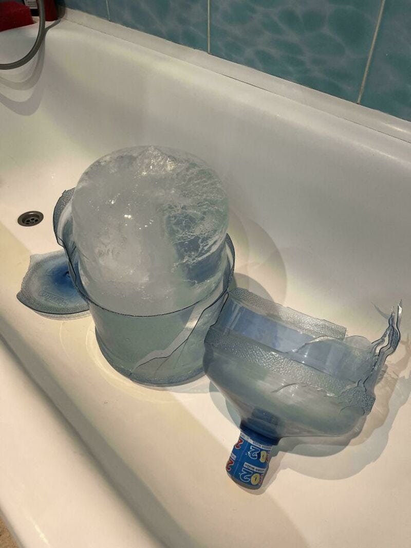 A plastic bottle with a large ice cube on top, placed in a bathroom sink.