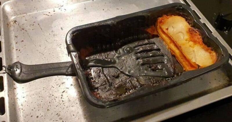 Burnt food in a black frying pan on a stove with a fork inside.
