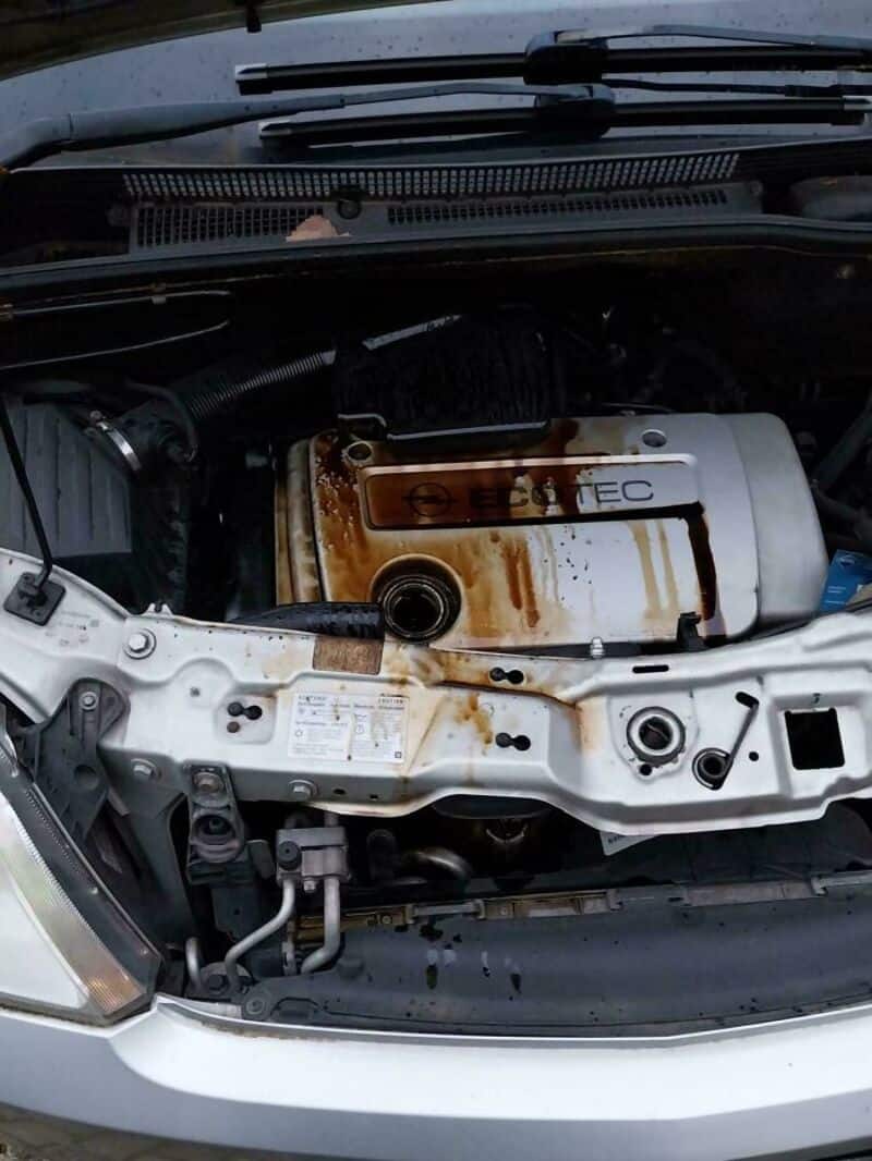 Car engine with rust and oil leak, hood open, under the windshield.