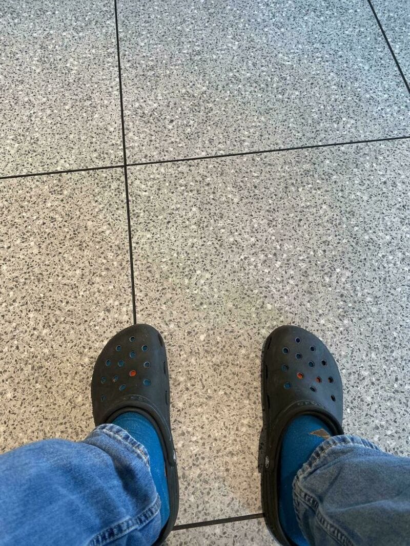 View of black Crocs shoes and blue jeans on tiled floor.
