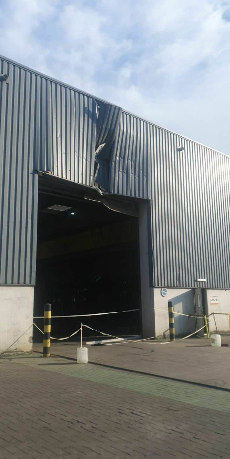 Damaged metal building with bent panels and a large opening.