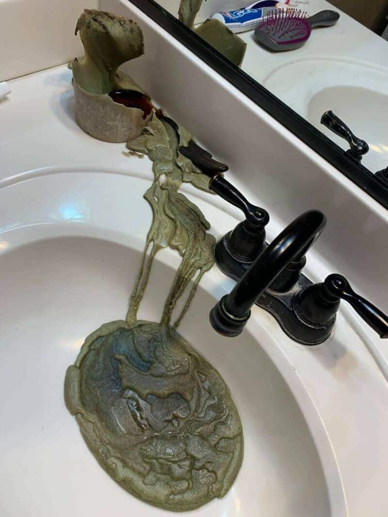 Clogged bathroom sink with greenish water and debris overflowing.