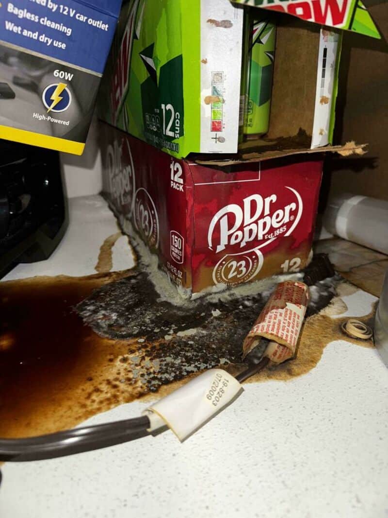 Spilled soda and broken box on cluttered countertop in a store or storage area.