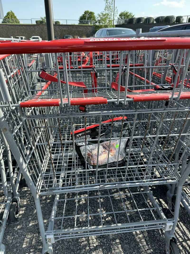 Empty shopping cart with a bag inside, parked in a lot with other carts and cars.