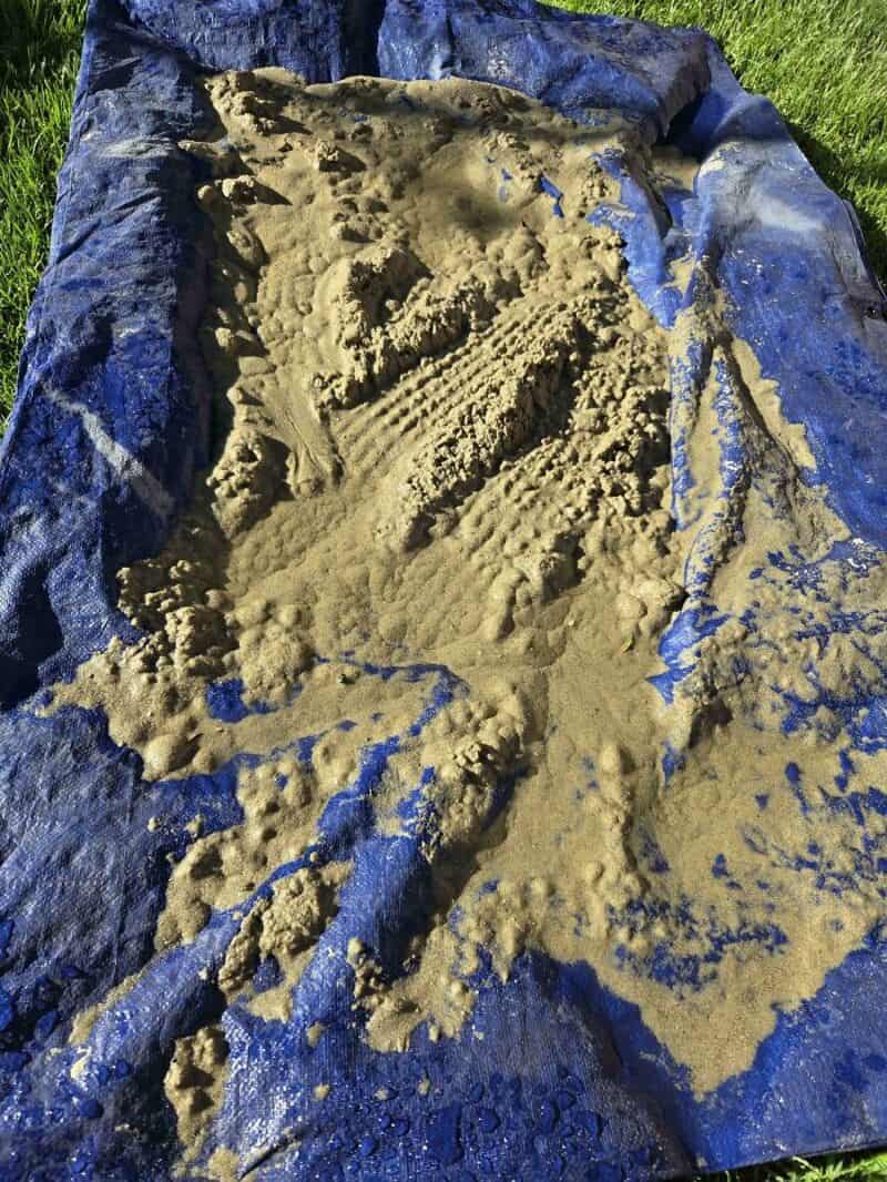 Sand on a blue tarp with footprints and uneven surface.