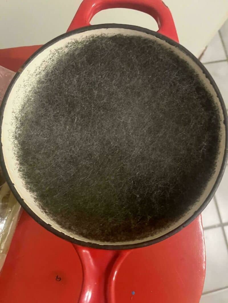 Burnt pan with blackened surface on red stove handle.
