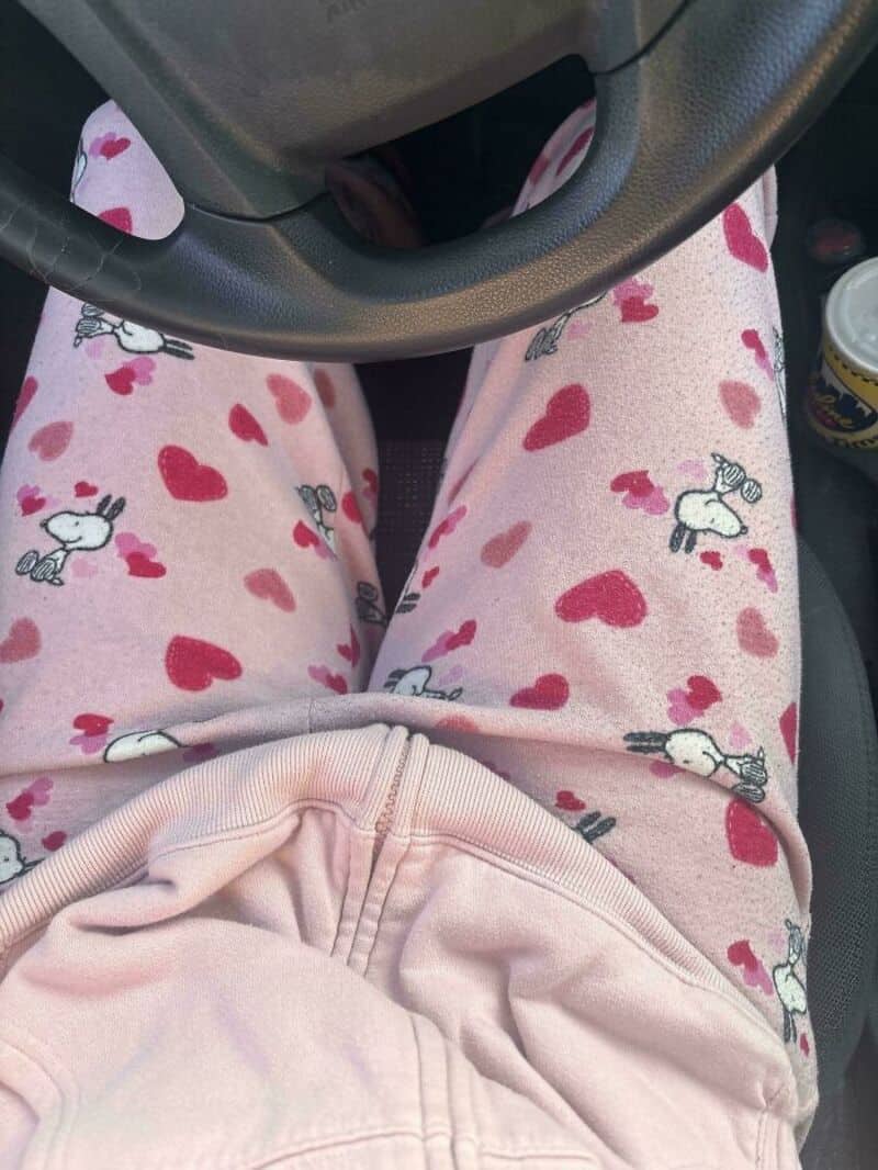 Person in pink pajama pants with hearts and unicorns, sitting in a car.