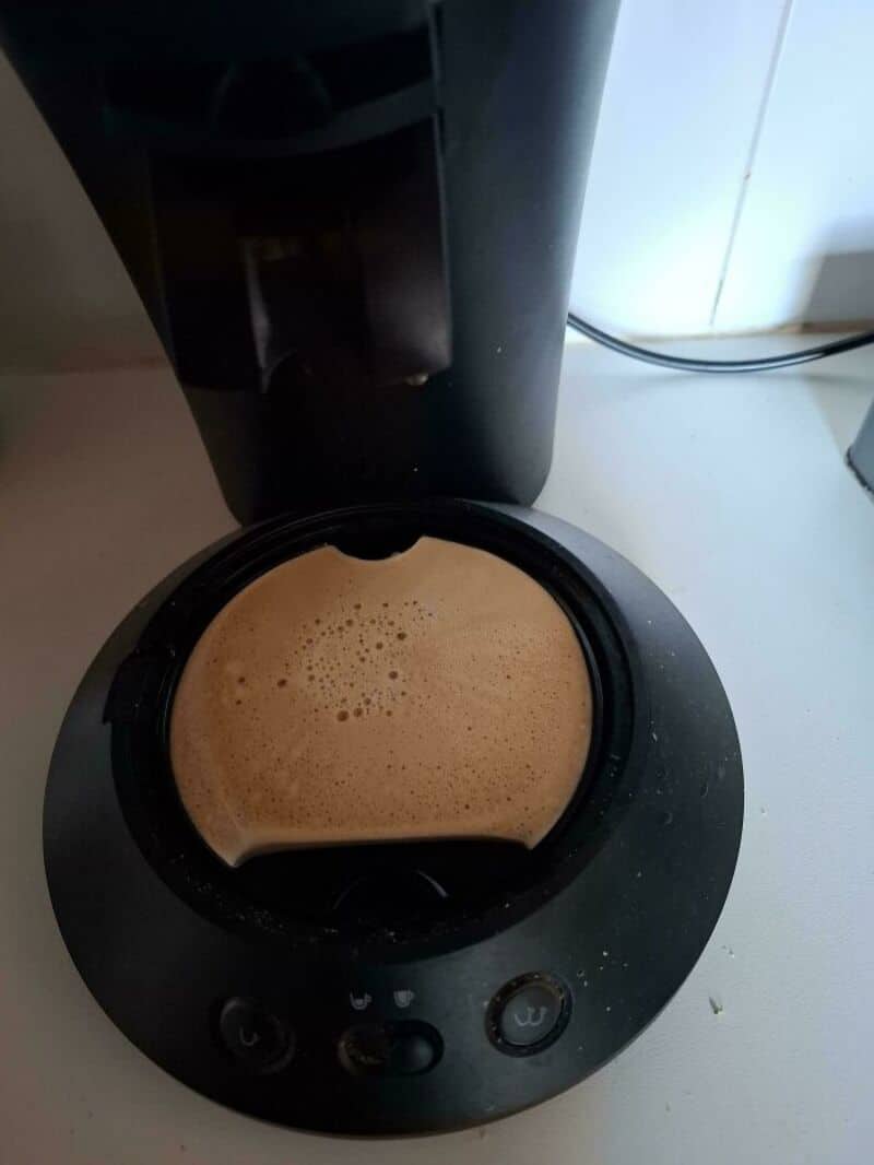 Coffee spilled in a black coffee maker, with foam and liquid inside.