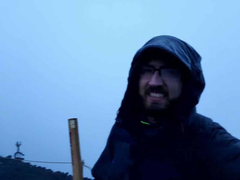 Person in rain gear taking a selfie on a foggy mountain summit.